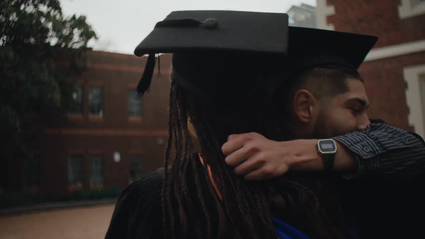 Happy man and woman in graduation gowns hugging each other