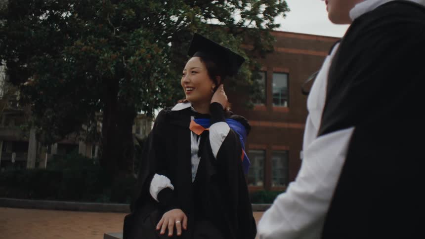 Graduate friends with graduation gowns chatting happily