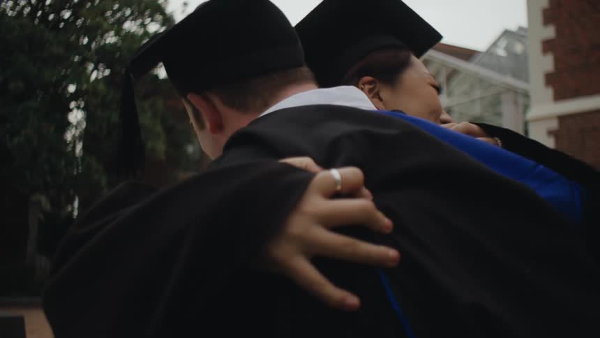 Graduate students wearing cap and gowns hug each other