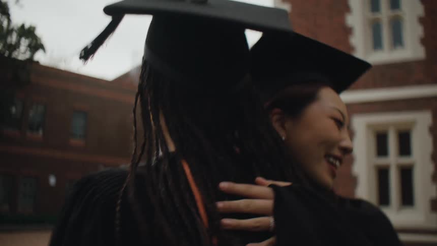 Two college students in graduation gowns hugging
