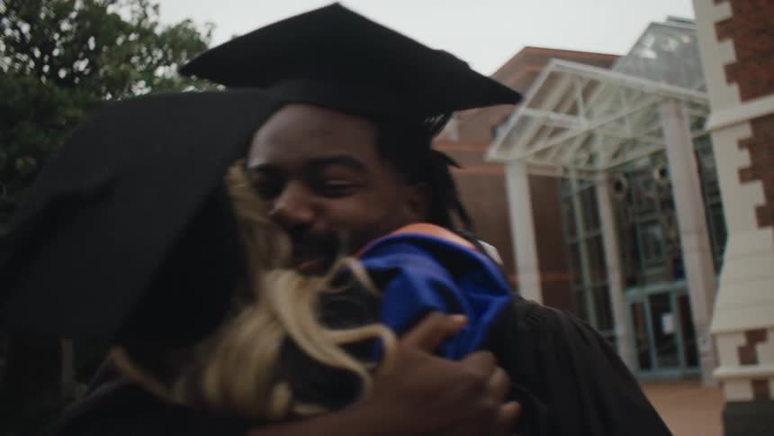 Two graduate students in cap and gown hug each other
