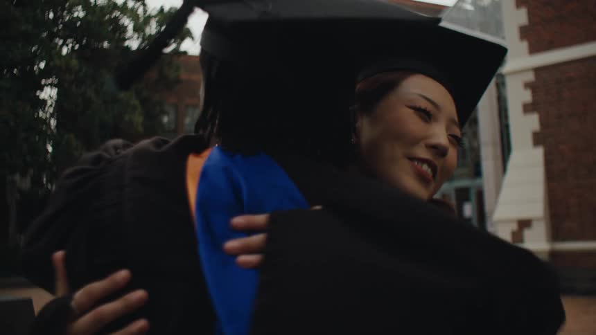 A group of people in graduation gowns and caps celebrate by hugging each other