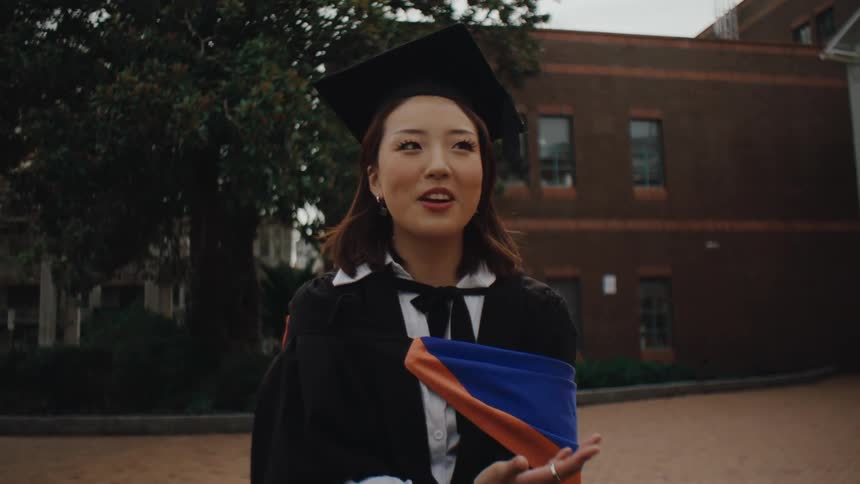 A graduate chats with someone on campus while wearing her cap and gown