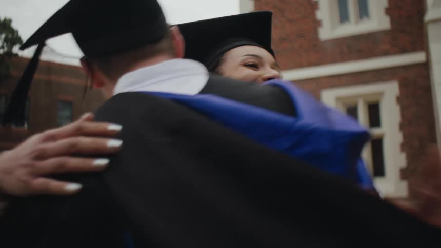 Graduate students wearing cap and gowns hug each other