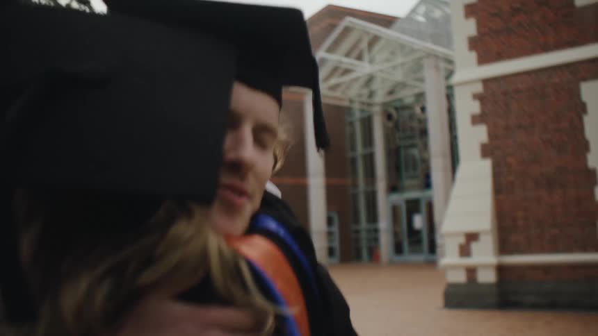 Blonde man and woman in graduation gowns hugging