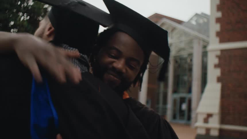 People in graduation gowns and caps celebrate by hugging each other