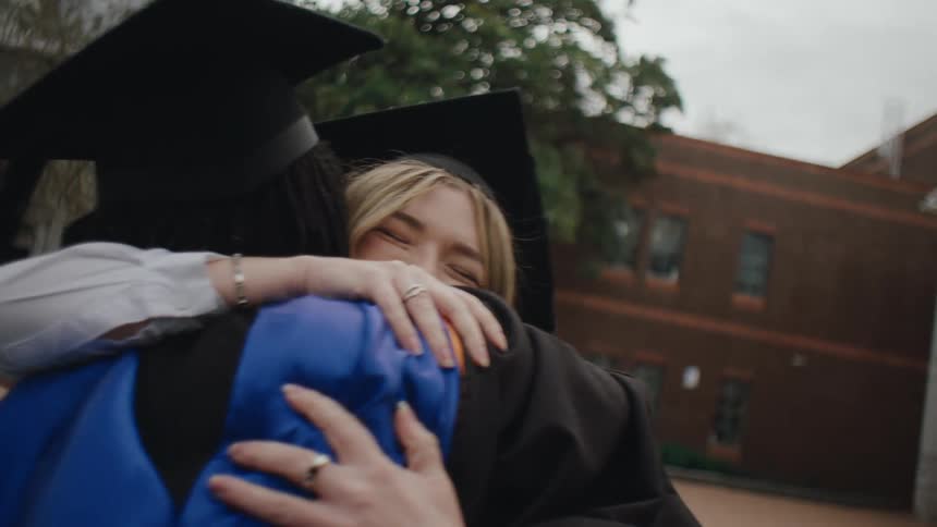 Two women happily hugging each other while wearing graduation attire