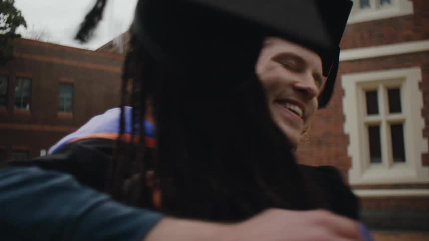 Two academics in graduation robes hugging each other