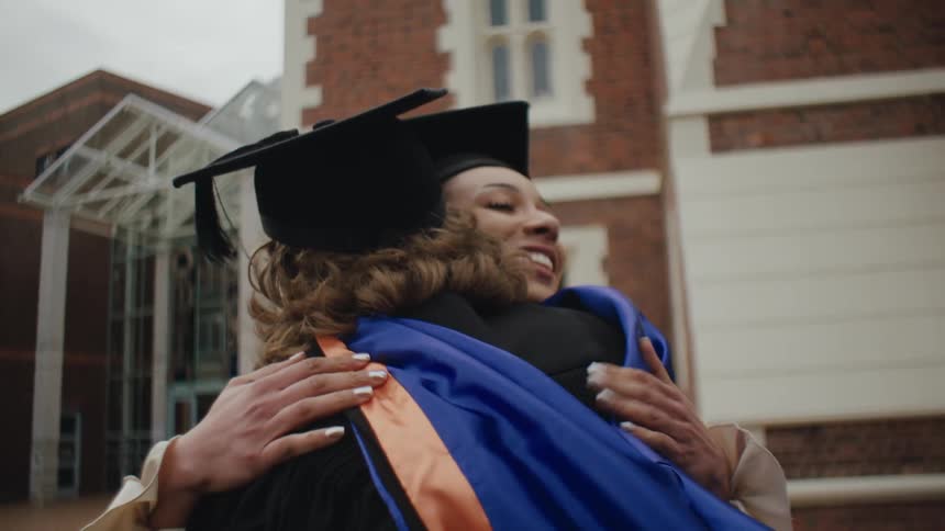A graduating student hugs a faculty member outside of a school building