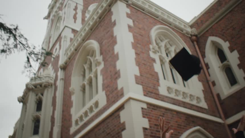 A student in graduation gown and cap celebrates by throwing her cap in the air