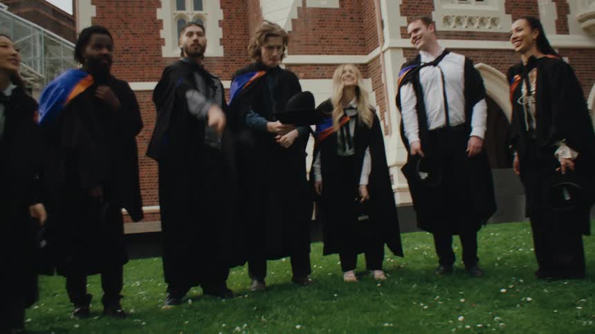 Students in graduation gowns taking off their hats and throwing them in the air