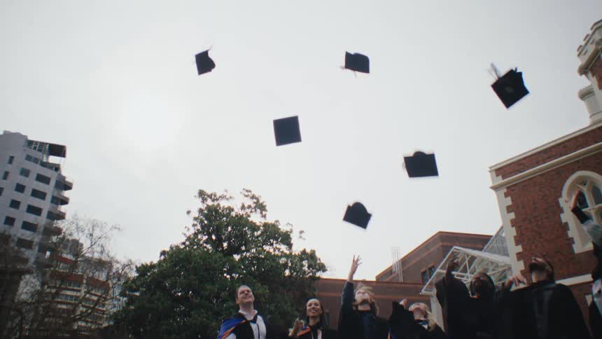 College graduates standing on the lawn throwing thier caps in the air