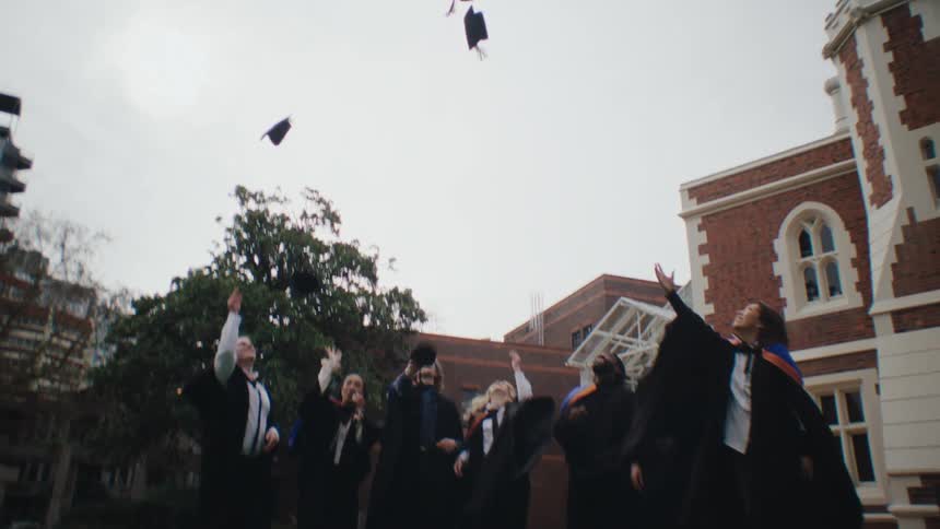 A group of people in graduation gowns and caps celebrate by throwing their caps in the air