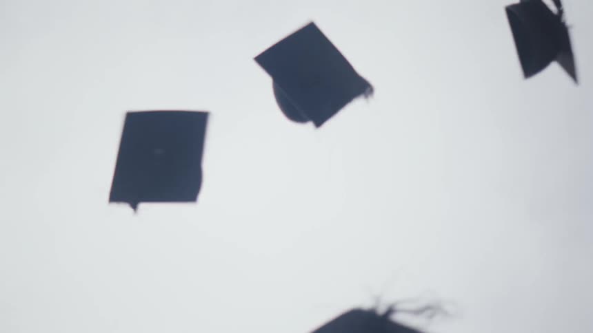A group of people in graduation gowns and caps celebrate by throwing their caps in the air