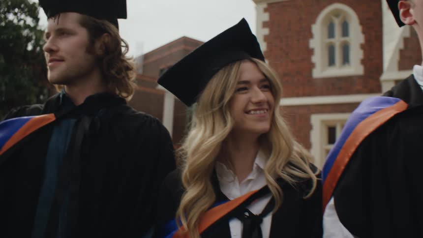 Graduating seniors smile while posing in their graduate robes near a campus building