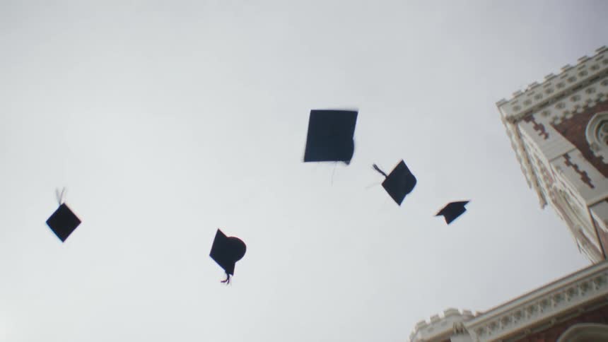 Group of university students all wearing graduation gowns throwing their hats in the air