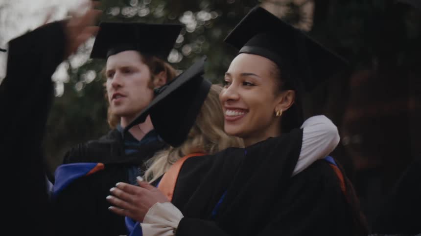 A group of people in graduation gowns and caps celebrate by hugging each other