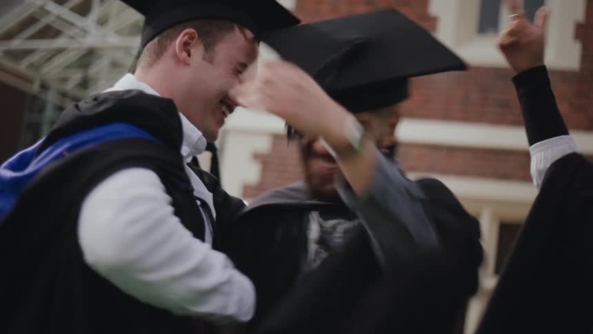 A group of people in graduation gowns and caps celebrate by hugging each other