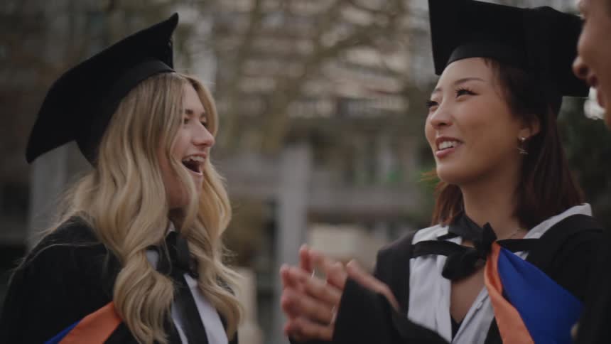 Three women in graduation gowns talking happily to each other