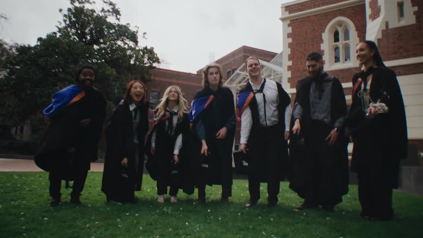 A group of people in graduation gowns and caps celebrate by throwing their caps in the air