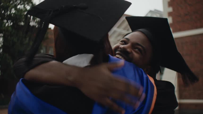 Students in graduation gowns greeting each other cheerfully with hugs