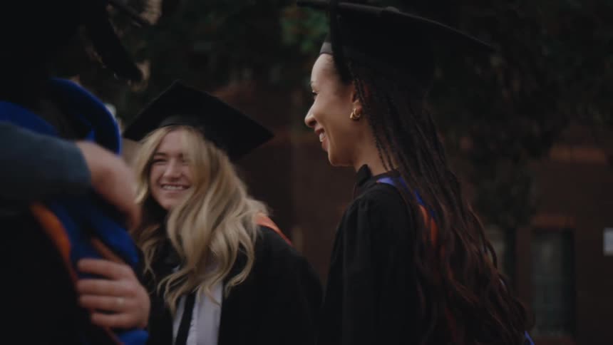 Group of college students wearing graduation gowns greeting each other