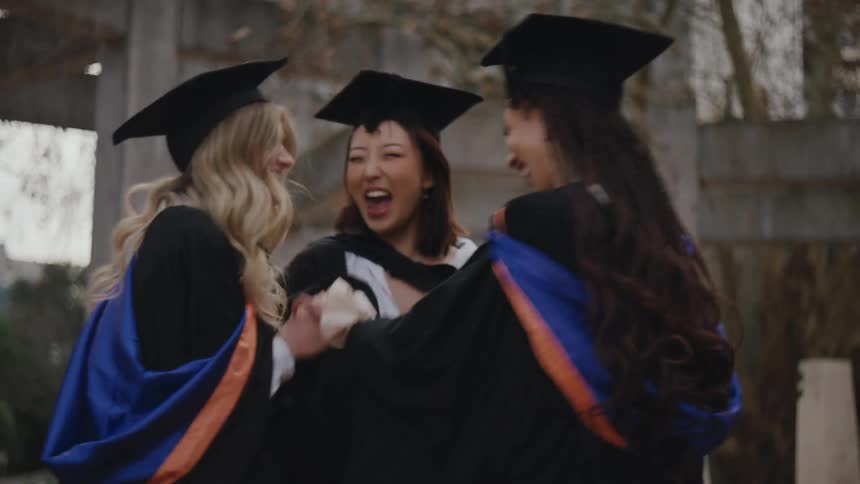 Three people in graduation gowns and caps standing together outdoors celebrating