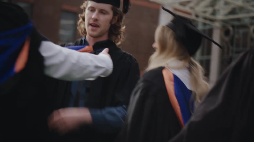 A group of people in graduation gowns and caps celebrate by hugging each other