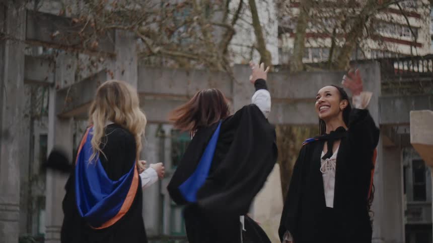 Friends in graduation gowns throwing their hats in the air