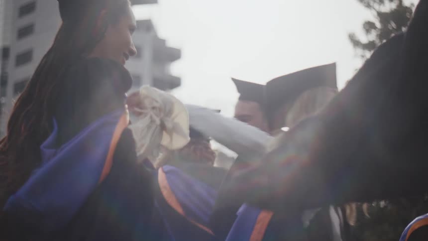 A group of people in graduation gowns and caps celebrate by hugging each other