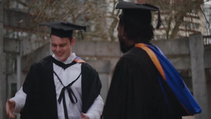 Group of four male students with graduation gowns talking to each other