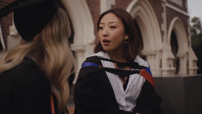 Two graduate students in caps and gowns talk outside the university
