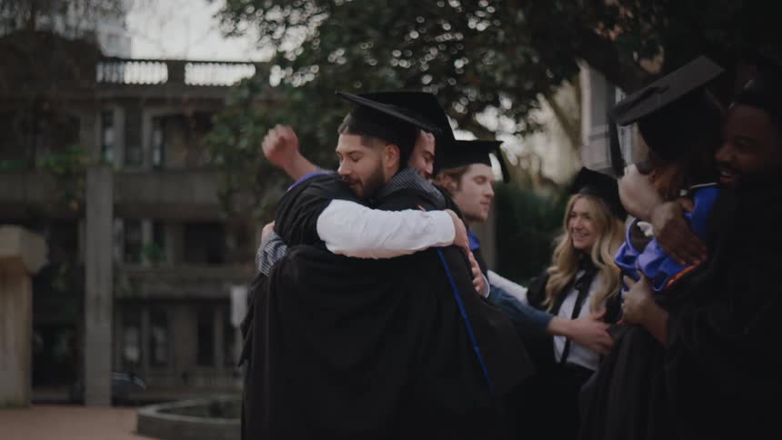 A group of students and a professor exchange hugs and smiles at a graduation ceremony