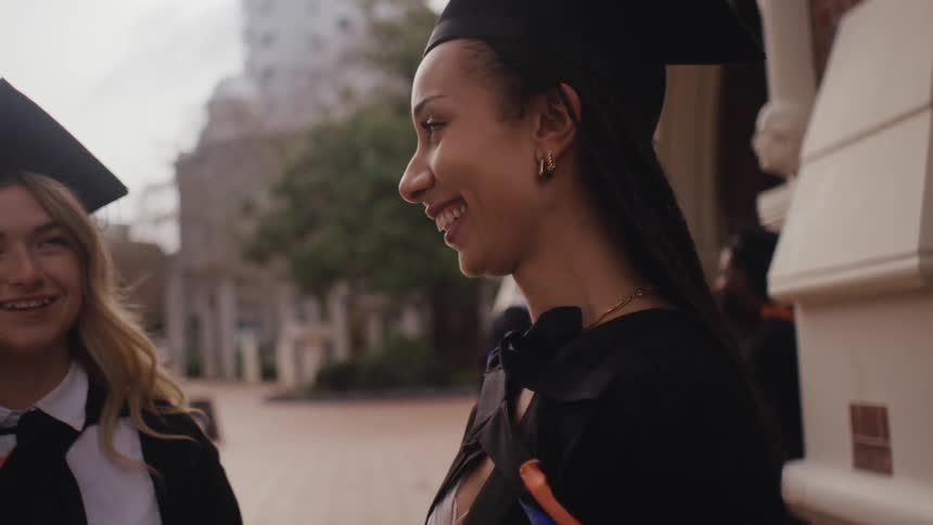 Smiling women talking to each other while everyone is wearing graduation gowns