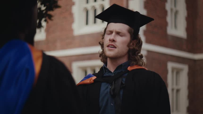 A young man and woman in graduation caps and gowns talk to each other