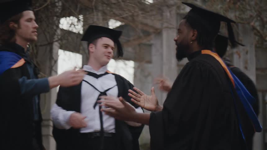 Men in graduation gowns touching hands and hugging each other