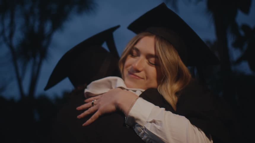 Two graduates in caps and gowns hold each other happily