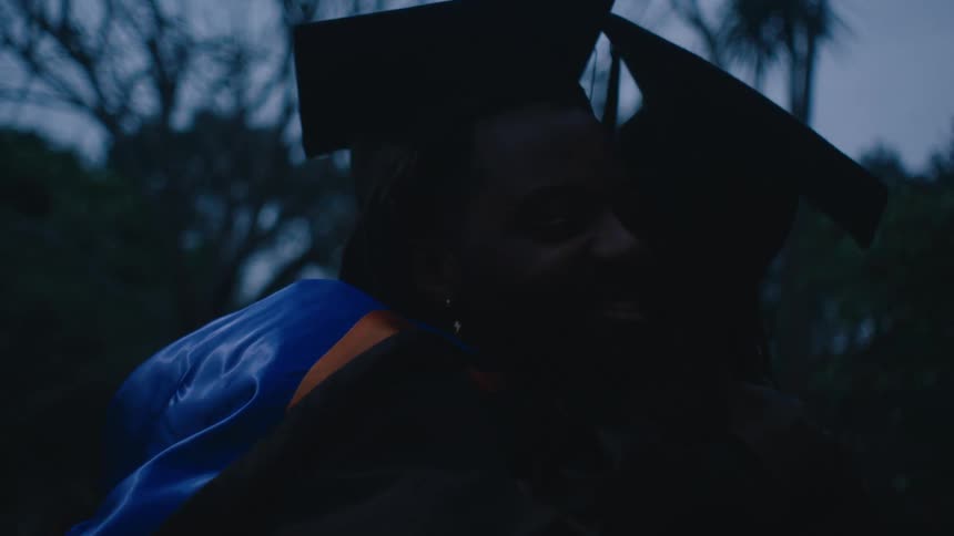A clip of two people in a graduation gown sharing a hug