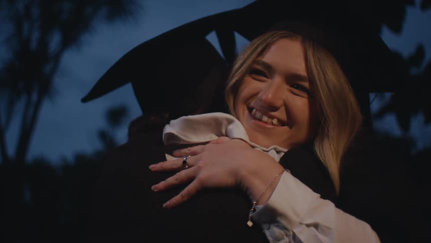 A woman in a graduation cap hugs someone happily