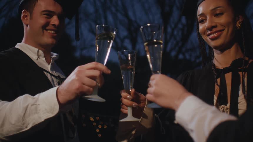 Three people toast with champagne flutes dressed in formal attire at nighttime