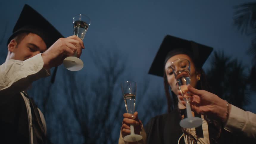Students in graduation gowns toasting champagne