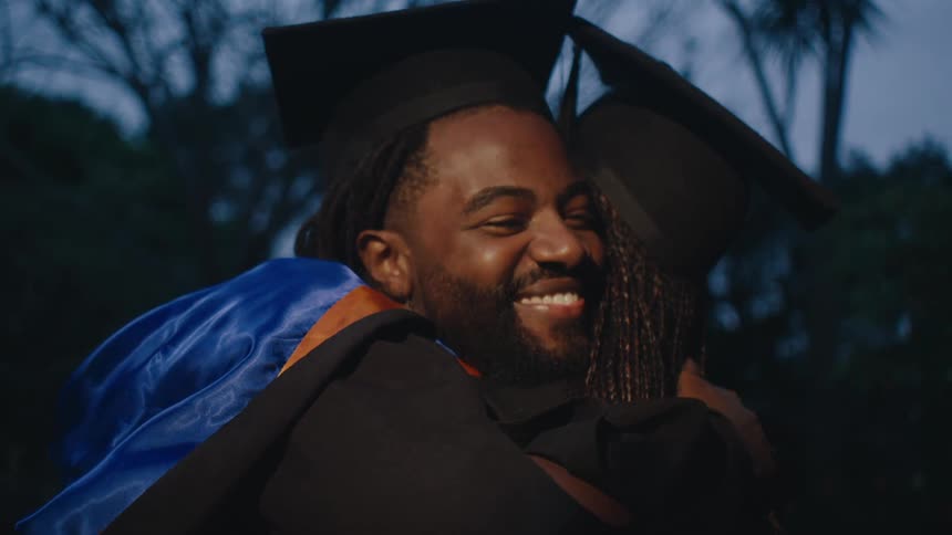 Two people happily hugging each other wearing graduation gowns