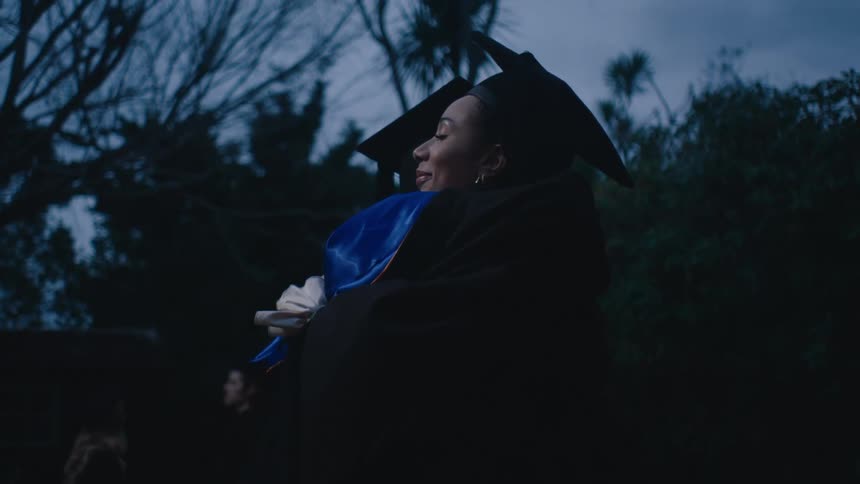 Two graduate students in cap and gown hugging each other