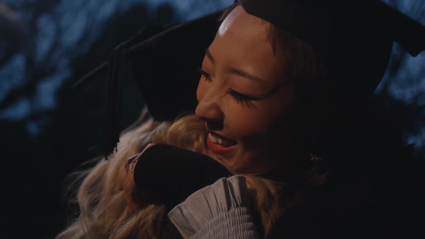 Two happy women both in graduation gowns hugging each other warmly