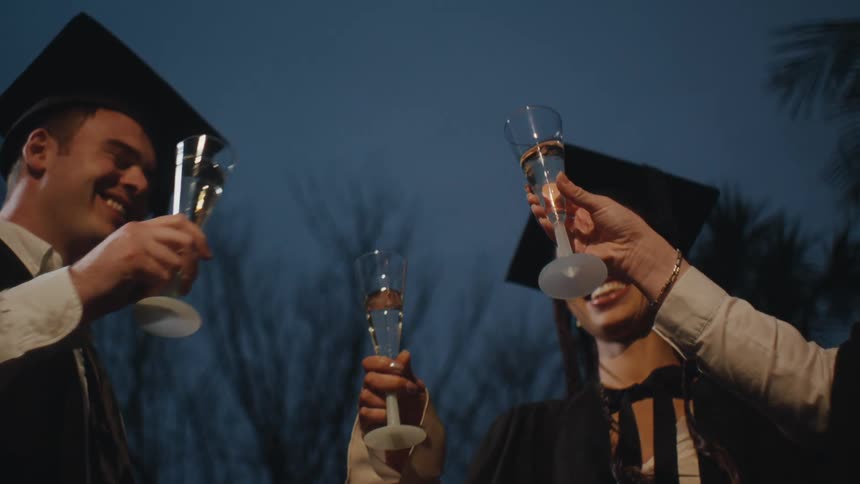 Three students in graduation gowns toasting with glasses of champagne