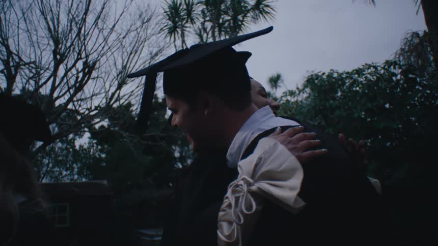 A group of people in graduation gowns and caps celebrate by hugging each other