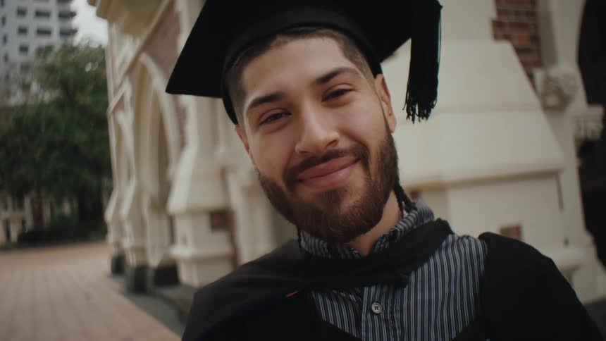 Graduating senior stands smiling near a campus building