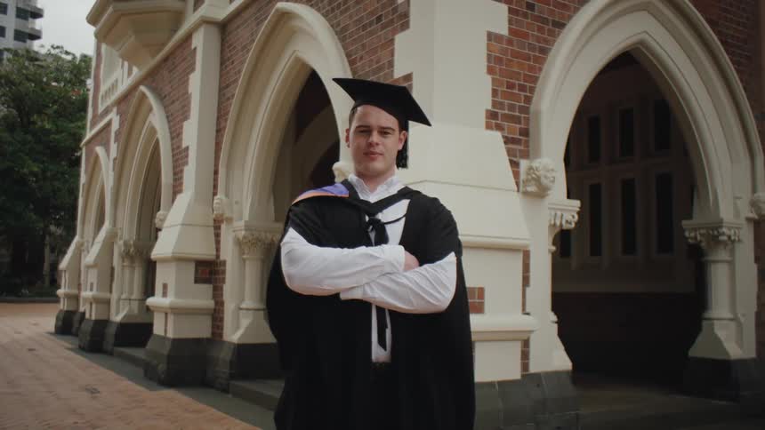 A graduate in cap and gown stands in front of an archedwindow building