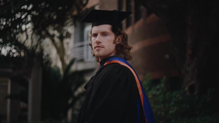 Man in graduation gown giving a slight smile