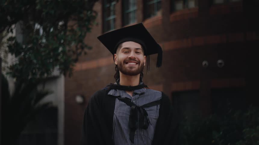 A young happy person with a beard wearing a black academic cap and gown